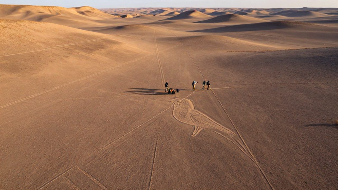 Un grupo de arqueólogos examina la superficie del desierto de Nazca junto al geoglifo de un colibrí y otras líneas ancestrales grabadas en el terreno.