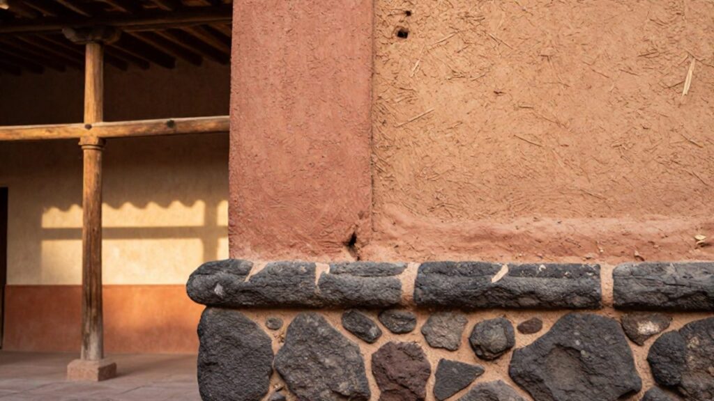 Detalle de la base de piedra andesita tallada que se une a una pared de adobe y una estructura de quincha con caña.